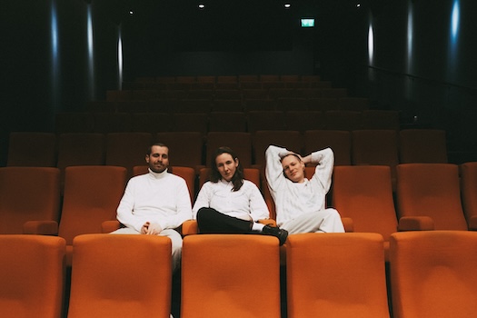 Alex, Lisa und Kenne sitzen nebeneinander in orangenen Kinostühlen